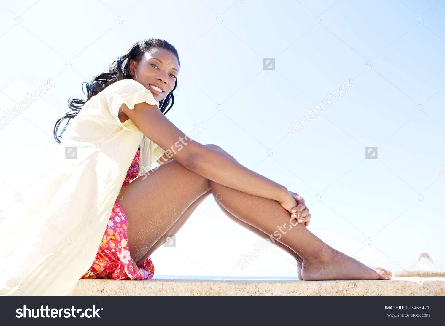stock-photo-low-view-of-a-beautiful-and-healthy-black-woman-sitting-against-a-bright-blue-sky-on-a-sunny-beach-127468421